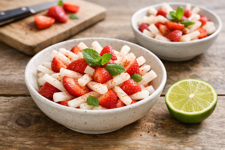Jícama sticks and sliced strawberries arranged loosely in a small wide bowl