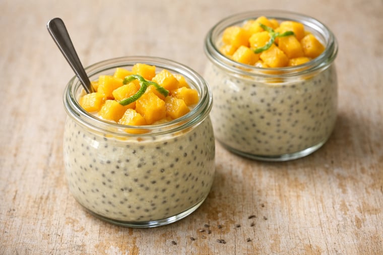 Two small wide-mouth glass jars on a worn light wood surface, filled with pale cream-colored chia pudding.