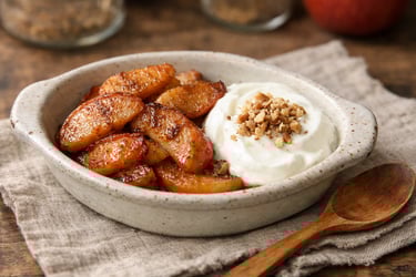 Manzanas asadas con canela servidas con yogur en un sencillo plato de cerámica.
